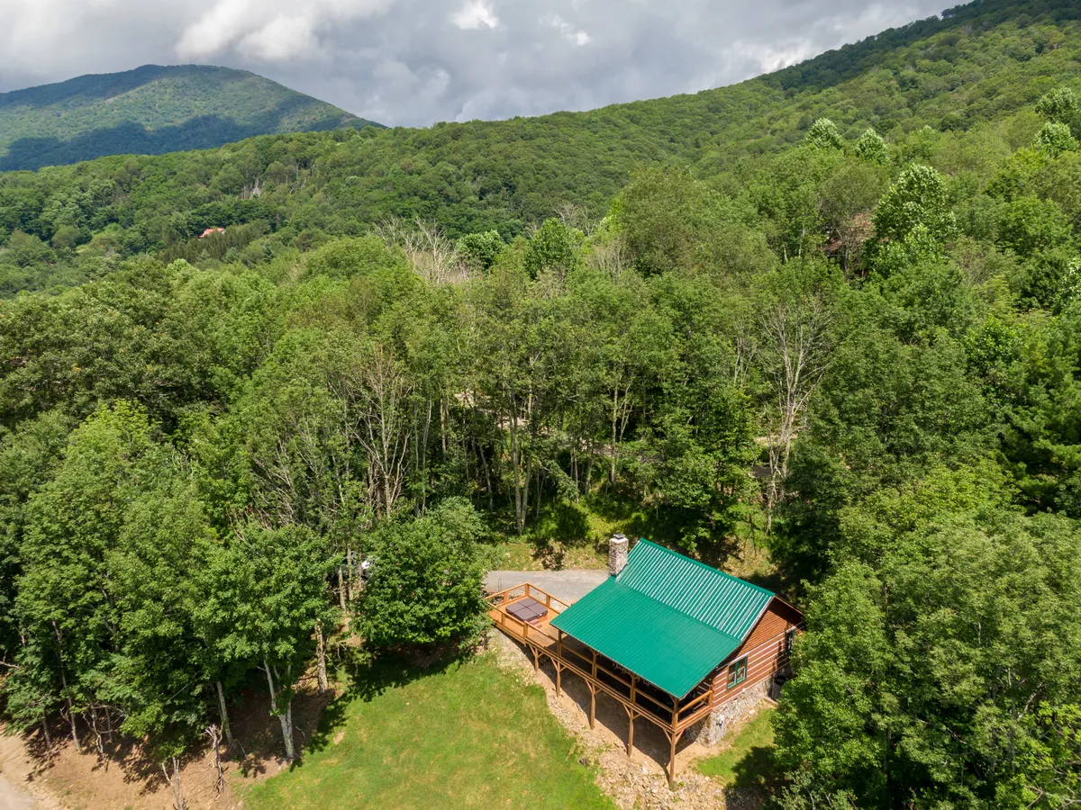 This image presents a classic cabin with a green metal roof nestled among trees, set against a stunning mountain backdrop. The porch invites guests to relax and enjoy the peaceful surroundings, and the scene evokes the adventure and tranquility of a mountain retreat.