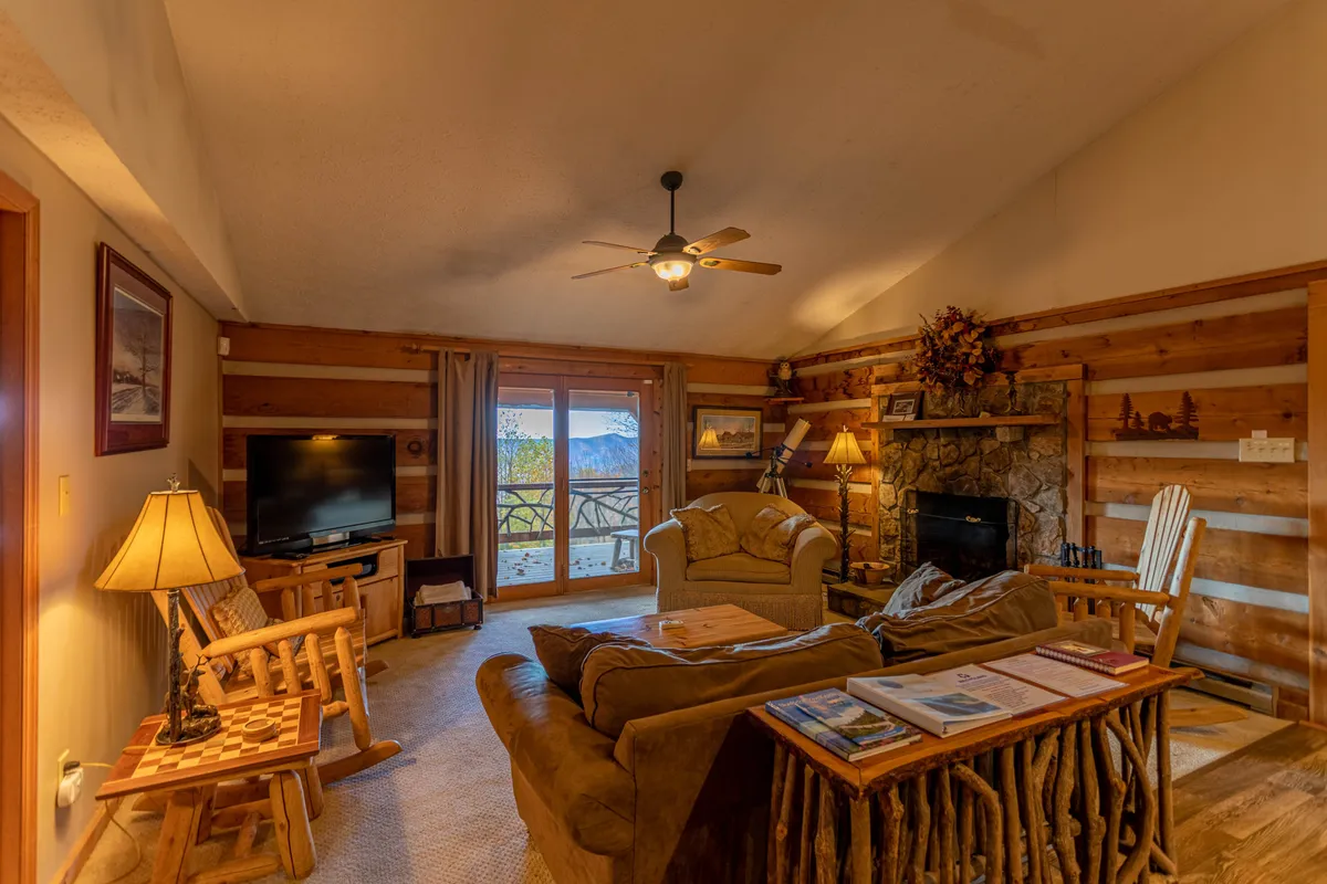 A warm and inviting living area centered on a stone fireplace, with comfortable seating facing a large window that frames a breathtaking mountain view. The space exudes a sense of coziness and serenity, making it ideal for intimate gatherings or quiet relaxation while staying connected with nature outside.