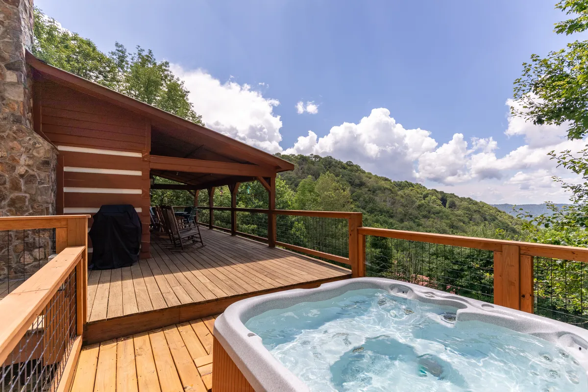 This exterior image captures a wooden deck featuring a hot tub and a pair of classic rocking chairs, all overlooking a vast mountain landscape. The soft light suggests evening, making the setting ideal for watching the sun set or stargazing in total privacy. The serene atmosphere is enhanced by the elevated vantage point and natural materials, reflecting the romantic and nature-focused escape described in the section.